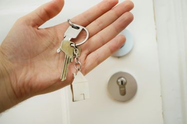 An open palm with keys resting on it, with a door in the background.