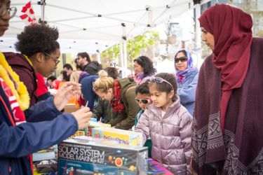 Image shows families visiting science exhibitions staffed by student volunteers.