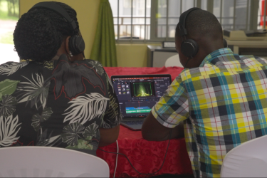Two men wearing earphones edit a video on a laptop