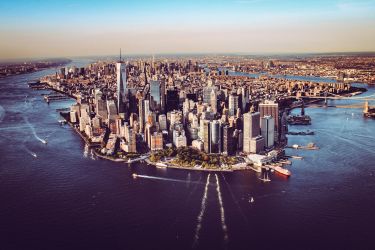 An aerial photo of Manhattan, New York City. You can see the iconic skyscrapers, the Hudson and East Rivers, and landmarks such as the One World Trade Center in the foreground and the Brooklyn and Manhattan Bridges in the distance.