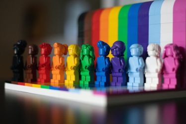 Rainbow colored Lego characters standing in front of a Pride flag background