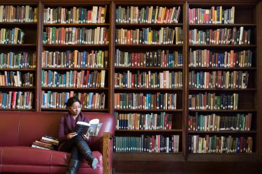 female alumni reading in the library surrounded by books
