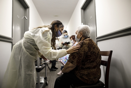 Nurse with hand on shoulder of elderly patient in hallway.