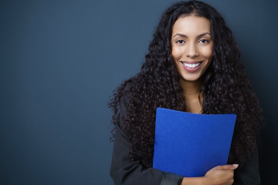 Black woman smiling holding a blue file folder.