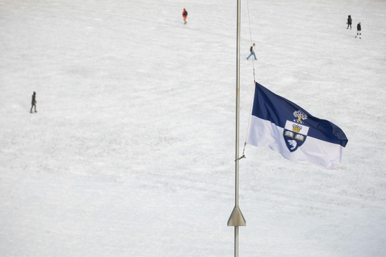 The U of T flag flies at half mast against the background of a snowy campus.