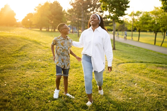 Thereasa Gordon and her young son laugh together, playing on a green hillside at sunset.
