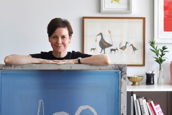 Alanna Cavanagh standing behind a desk in front of her artwork. 