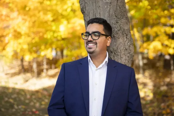Amit Dalaya in a blue blazer standing under fall trees with yellow leaves