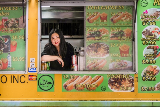 Joanna Luo smiles as she looks out the window of a food truck plastered with prices and images of burgers and fries.