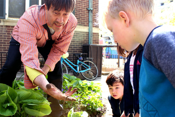 Standing in a garden, Doug Anderson shows children his hand filled with soil and a worm.