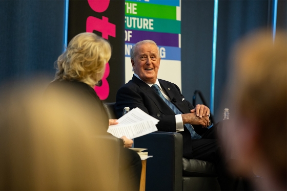Brian Mulroney smiles as he sits in a chair on stage chatting with a moderator.
