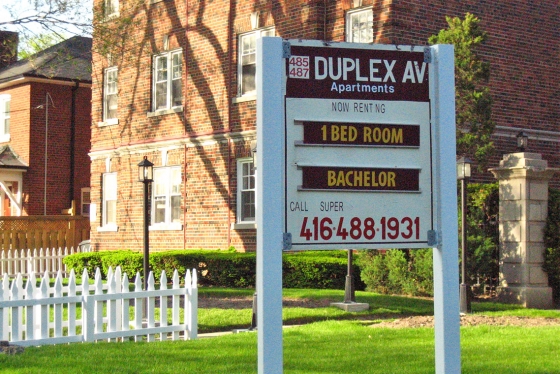 A sign outside a brick building reads: 485/487 Duplex Ave, now renting, 1 bedroom, bachelor, call super 416-488-1931.