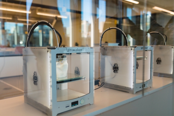 A row of 3D printers: plastic and metal boxes with a transparent front and a movable shelf inside.