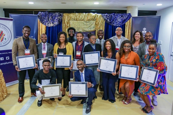 A group of 15 people pose holding framed African Scholars Awards certificates.
