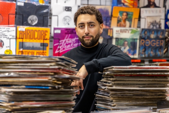 Amir Alam posing behind two tall piles of vinyl records