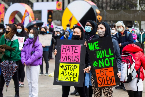 A crowd of people in masks at a protest hold signs that read: Hate is a Virus, Stop Asian Hate, We will not be silent.