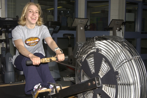 Kaley McLean smiles as she sits on a piece of homemade gym equipment featuring foot pedals, a wheel and a handhold.