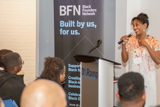 Rhonda McEwen speaks in front of a sign that says: BFN, Black Founders Network, built by us, for us.