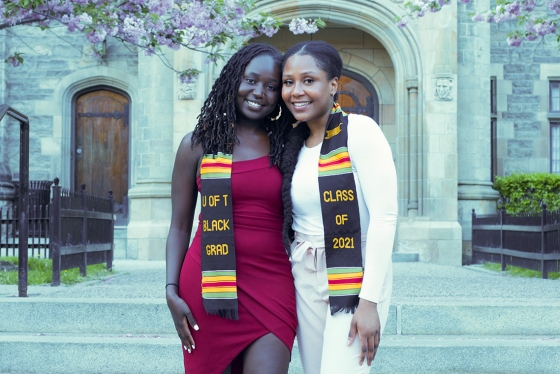 Cindy Njoki Kamau and Debora Oresajo smile together, wearing kente scarves that read: U of T Black Grad Class of 2021.