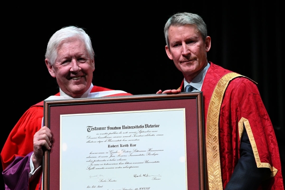 Bob Rae poses with Victoria University Chancellor Nick Saul and a large framed diploma.