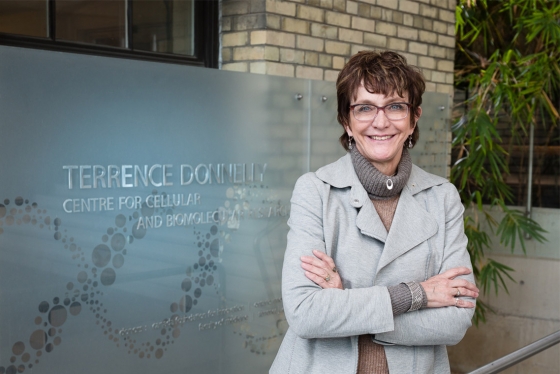 Brenda Andrews smiles as she stands beside a sign reading Terrence Donnelly Centre for Cellular and Biomolecular Research