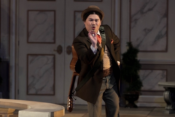 Danlie Rae Acebuque in costume as Figaro. He is singing and gesturing, wearing a guitar slung on his back.