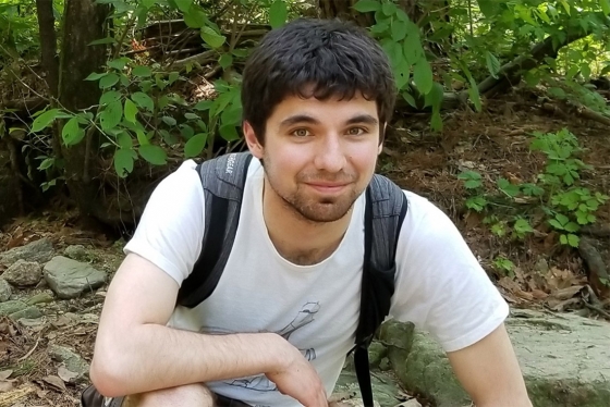 Erik Etzler smiles as he crouches on a forest trail, wearing a backpack.