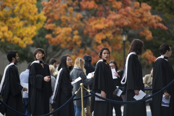 Graduates line up outside Convocation Hall in front of the fall foliage