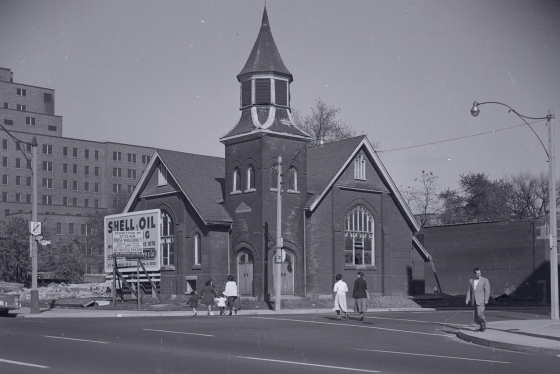 Archival photograph of First Baptist Church in the 1950s, squeezed next to a construction site and a billboard for Shell Oil.