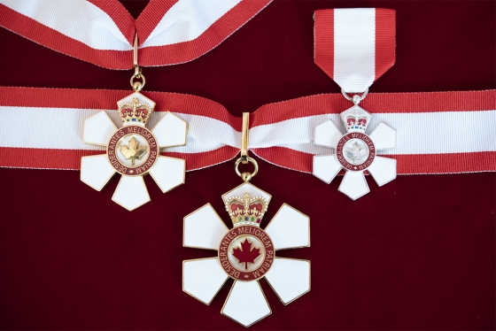 Three six-petalled Order of Canada medals hanging on ribbons in the colours of the Canadian flag.