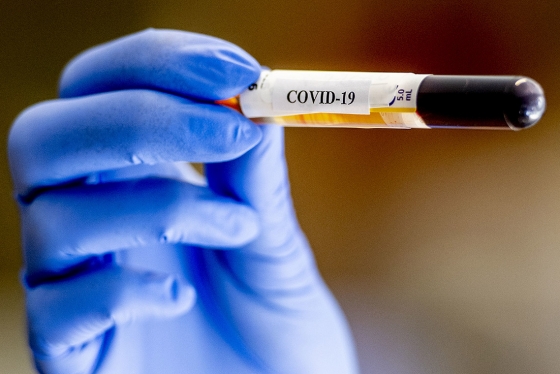 A gloved hand holds a medical vial labelled COVID-19.