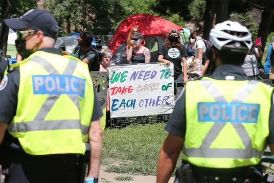 Police face protesters holding a sign that reads: We need to take care of each other.