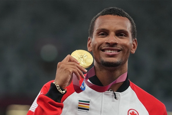 Andre De Grasse smiles as he holds up an Olympic gold medal.