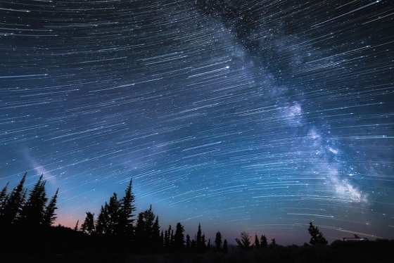 In a time-lapse image, thousands of stars appear as streaks of light across a dark sky and the cloudy line of the Milky Way.