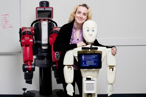 Goldie Nejat stands with a human-shaped robot. Text on the robot’s chest: Autonomous Systems and Biomechatronics Lab.