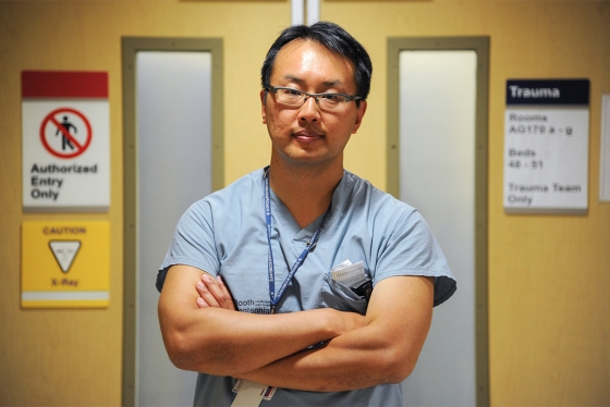 Homer Tien stands with arms folded in a hospital corridor, by the door to the Trauma room.