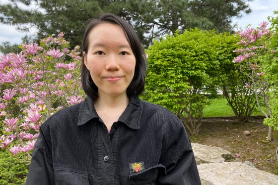 Irene Fang stands outside with trees and flowers around her