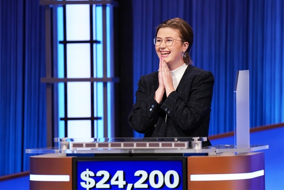 Mattea Roach smiles and claps, standing at a Jeopardy podium. The dollar total on her screen reads $24,200.