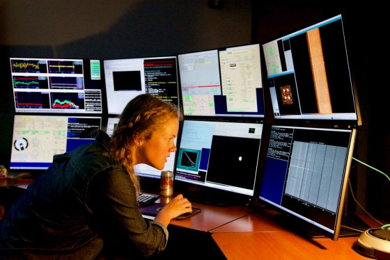 Katie Harris works in front of a bank of eight computer monitors, all displaying different information.