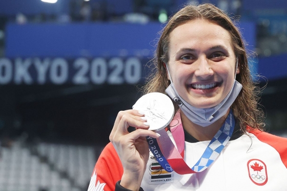 Kylie Masse smiles as she holds up her Olympic silver medal. A banner behind her reads: Tokyo 2020.