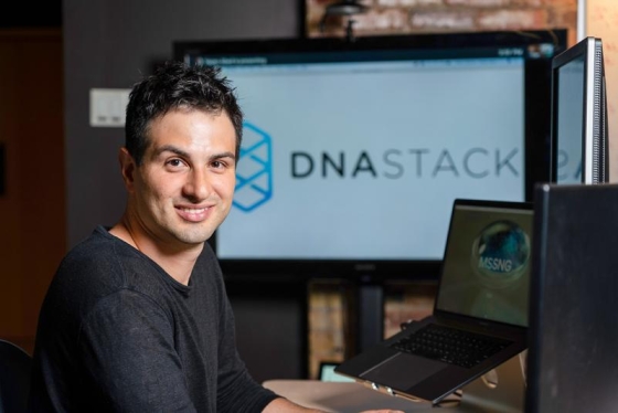 Marc Fiume smiles as he looks away from an array of computer monitors displaying the logo of his company DNAstack.