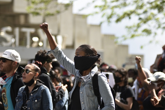 A young woman in a mask holds her fist in the air. Behind her is a crowd of other protesters on University Avenue in Toronto.