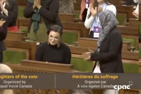 In Ottawa's House of Commons, women stand and applaud Riley Yesno. Caption reads: Daughters of the vote, Equal Voice Canada.