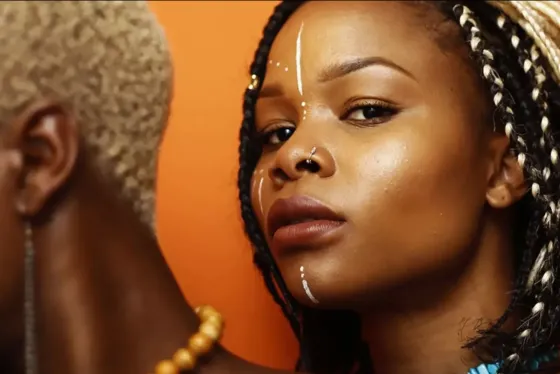 An artistic photograph of a woman with lines of white paint on her face and braids