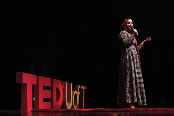 Salma Hindy talks into a microphone on a stage. Large letters behind her read, TEDx U of T.