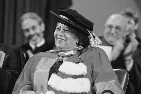 Toni Morrison smiles, wearing academic robes and a hat as she sits on stage at Convocation Hall after receiving an honorary degree