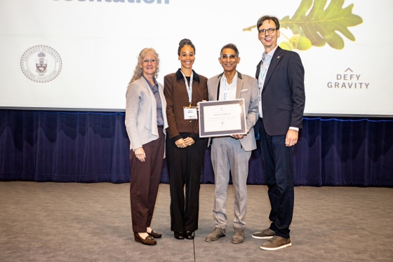 Dr. Vivian Rambihar accepts his award on stage from three other people, Carl Mitchell's wife Margaret Shaw, daughter Nancy Mitchell and UTAA President Corwin Cambray.