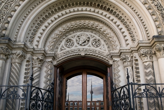 The Toronto skyline with CN Tower is reflected in a door framed by an elaborately carved stone archway.
