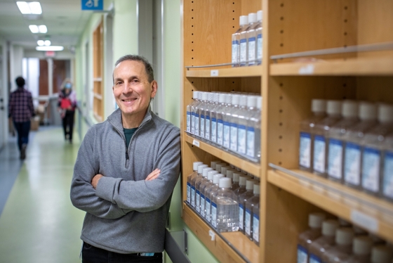 Daniel Druckers smiles and leans on a shelf of labelled bottles.
