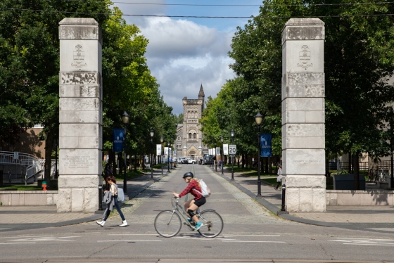 Pedestrians walk past the Alumni Gates on U of T's St. George campus. University College is pictured in the background. 